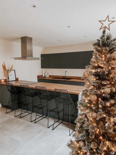 kitchen of MySymphonyStyle November winner. A dark grey anthracite kitchen with wood worktops and black barstools at a breakfast bar. A pampas grass vase features on the bar alongside a photo frame. A christmas tree features in the corner of the image decorated with fairy lights and baubles