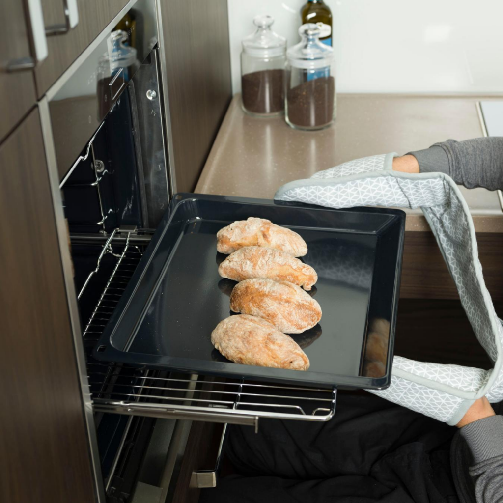 Oven is open wth shelf underneath and bread is been taken out the oven on a baking tray